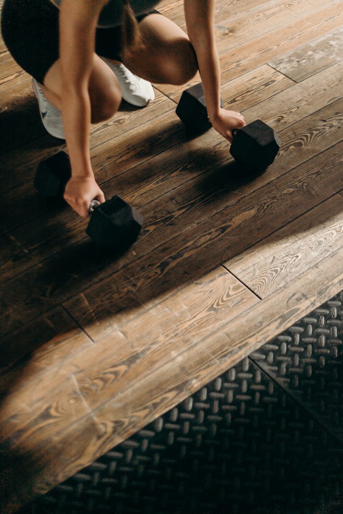Female gym-goer in action with dumbbells on wooden floor, ready to lift.