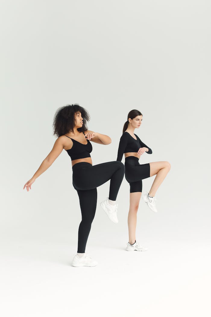 Two women perform fitness exercises in a minimalist studio setting, emphasizing strength and balance.