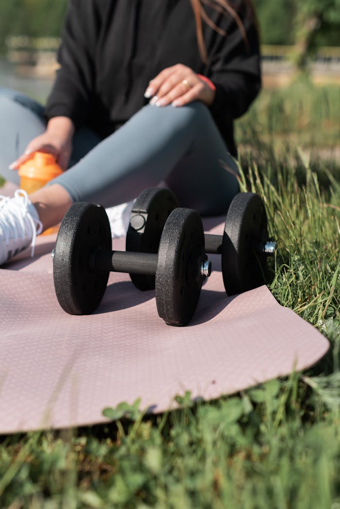 Woman exercising with dumbbells outdoors on a yoga mat.